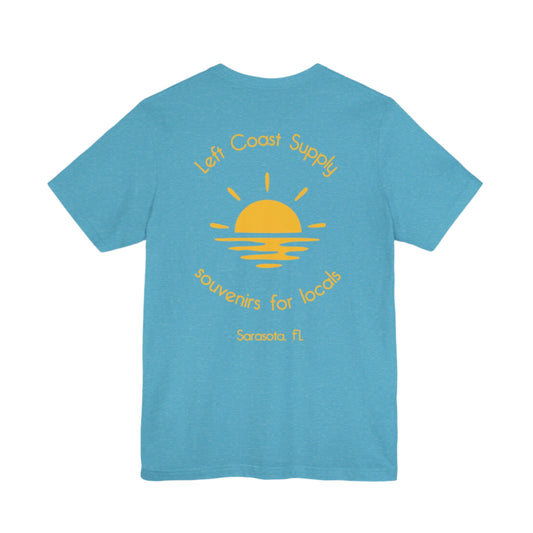 Blue t-shirt with yellow graphic of sunset with souvenirs for locals written. Left Coast Supply