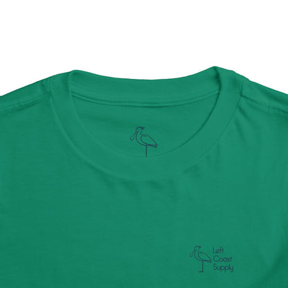 Green toddler T-shirt with the text 'Kiss Me I'm Ibis' and an illustration of an ibis bird and a pot of gold. Left Coast Supply