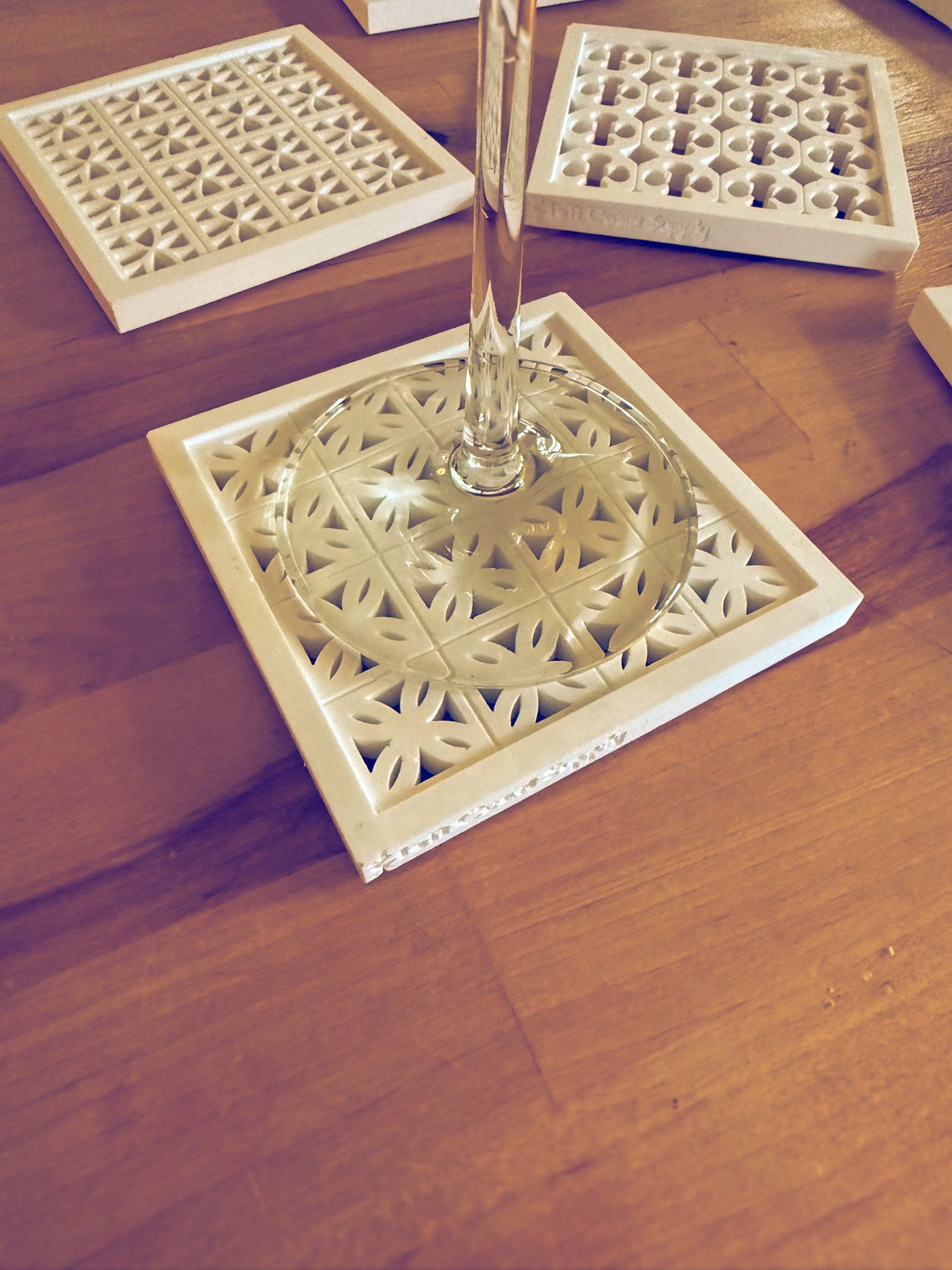 A detailed white patterned coaster beneath a glass on a warm wooden table